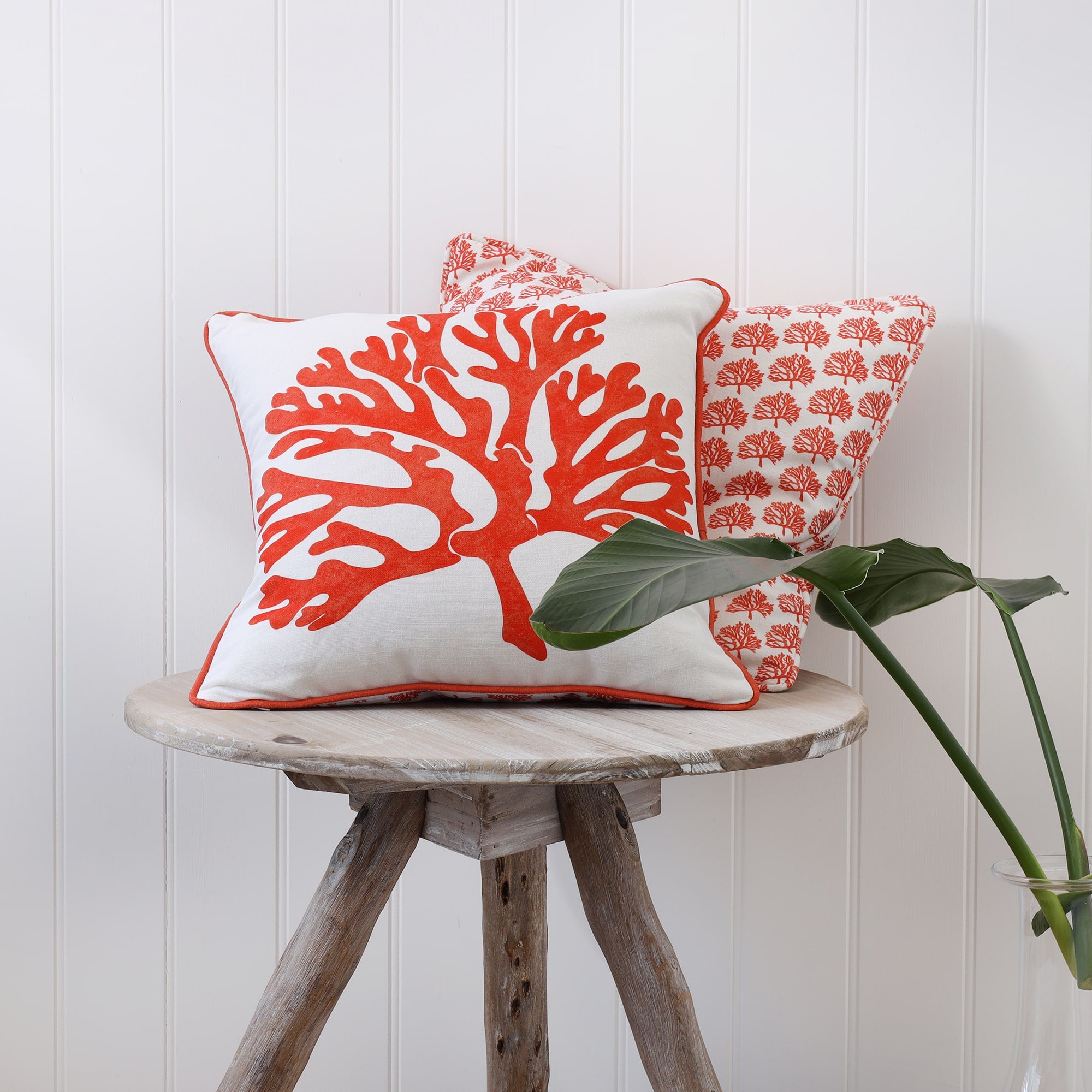 Orange mini coral cushion behind a cushion with a larger print on the front,both are placed on a tripod table.