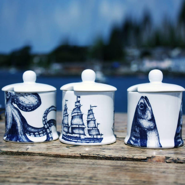 Jam Pots with lid in our classic range in the Mackerel design,Octopus and Packetship with a space in the lid for a tea spoon,all three are on a wooden table with the harbour's edge in the background