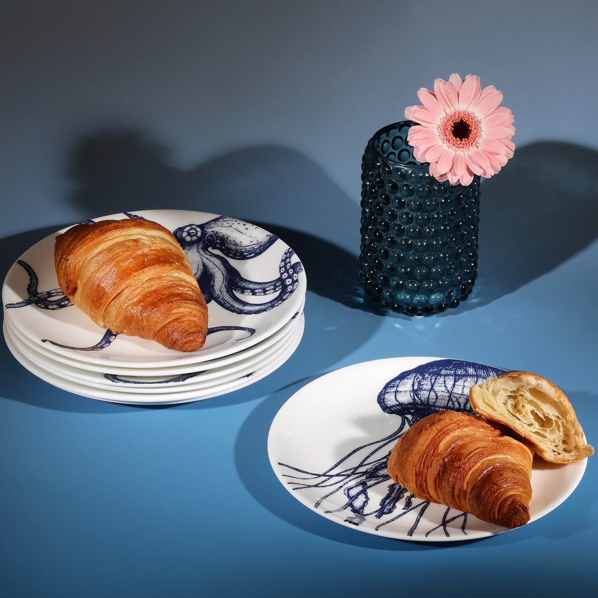 Stacked bone china side plates decorated with croissants next to a petrol blue candle holder
