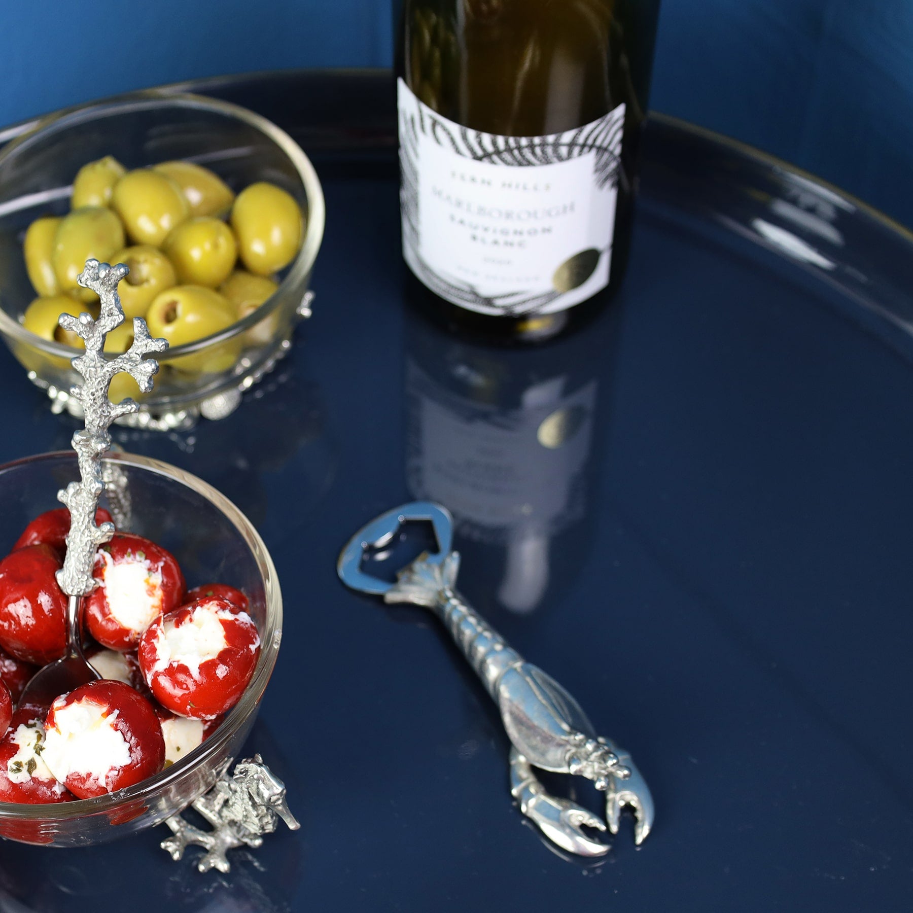 Pewter Lobster shaped Bottle Opener placed on a table with other pewter items on the table and a wine bottle in the background