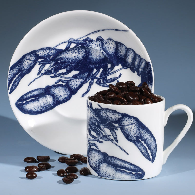 Bone China white espresso cup in hand drawn illustration in our Lobster design in Navy with matching saucer.Saucer is standing on its side with the coffee cup in front filled with coffee beans