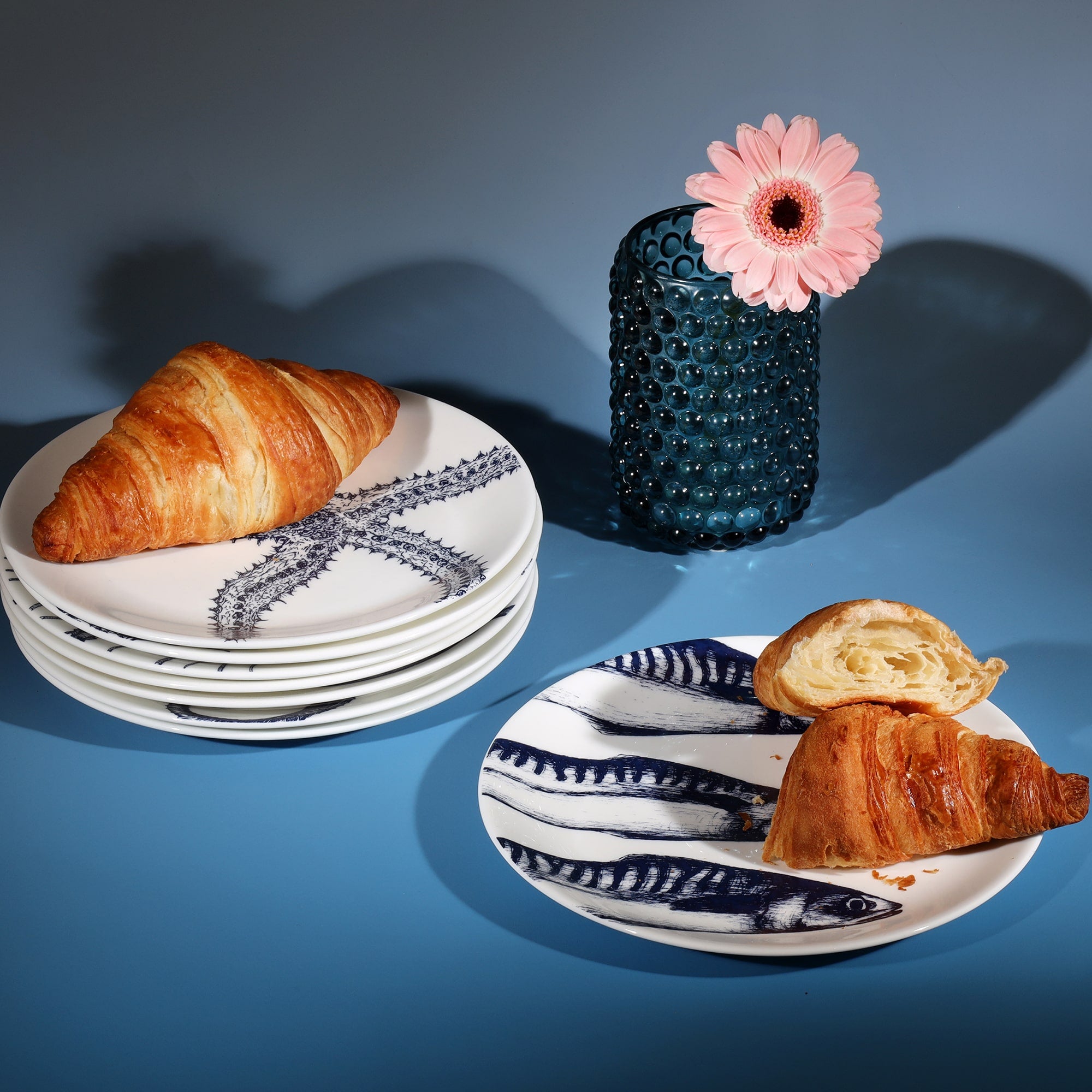 Stacked bone china side plates decorated with croissants next to a petrol blue candle holder