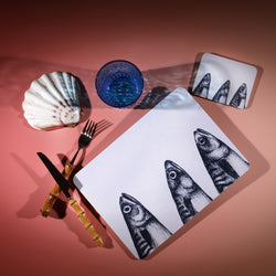 Mackerel Heads  Design in Navy on a white Coaster with a matching Placemat.On the table is a bamboo cutlery set and a blue coloured glass