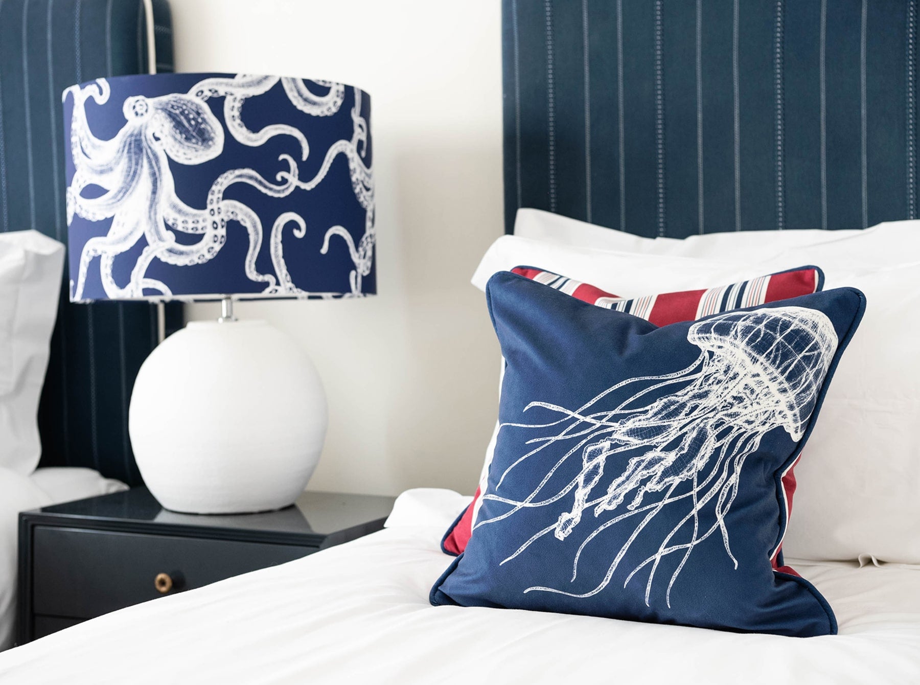 Our Classic Octopus White design on a Navy background on a White lampbase placed on a navy bedside table in between two single beds. One of the beds have our classic designs placed on.