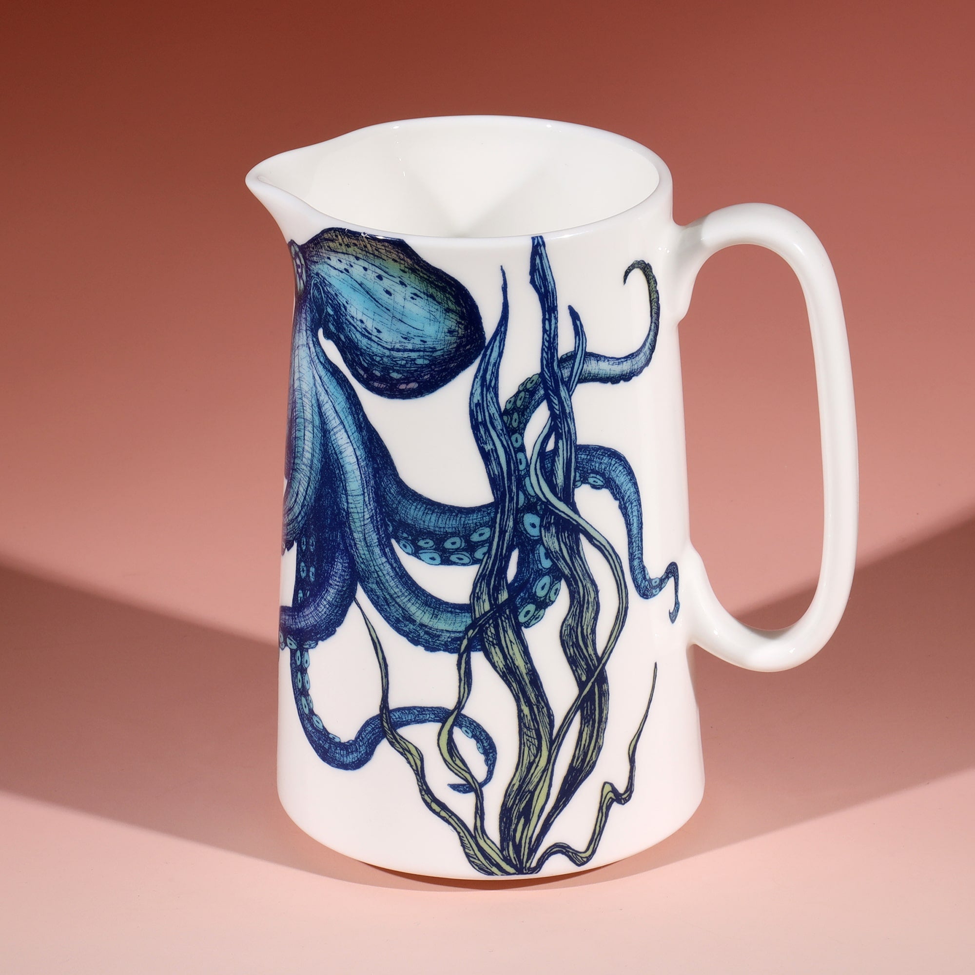 White jug with a brightly coloured blue and green octopus and seaweed design on a graduated coral coloured background. 