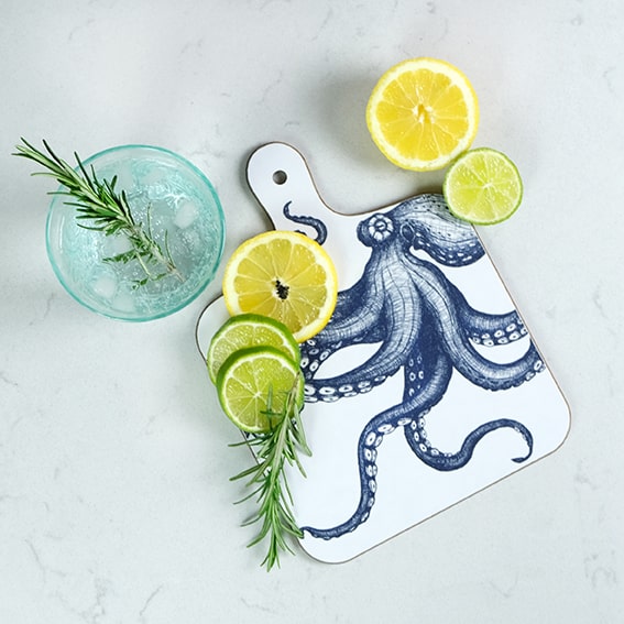 Octopus mini chopping board placed on a table with lemon and limes next to a glass filled with ice