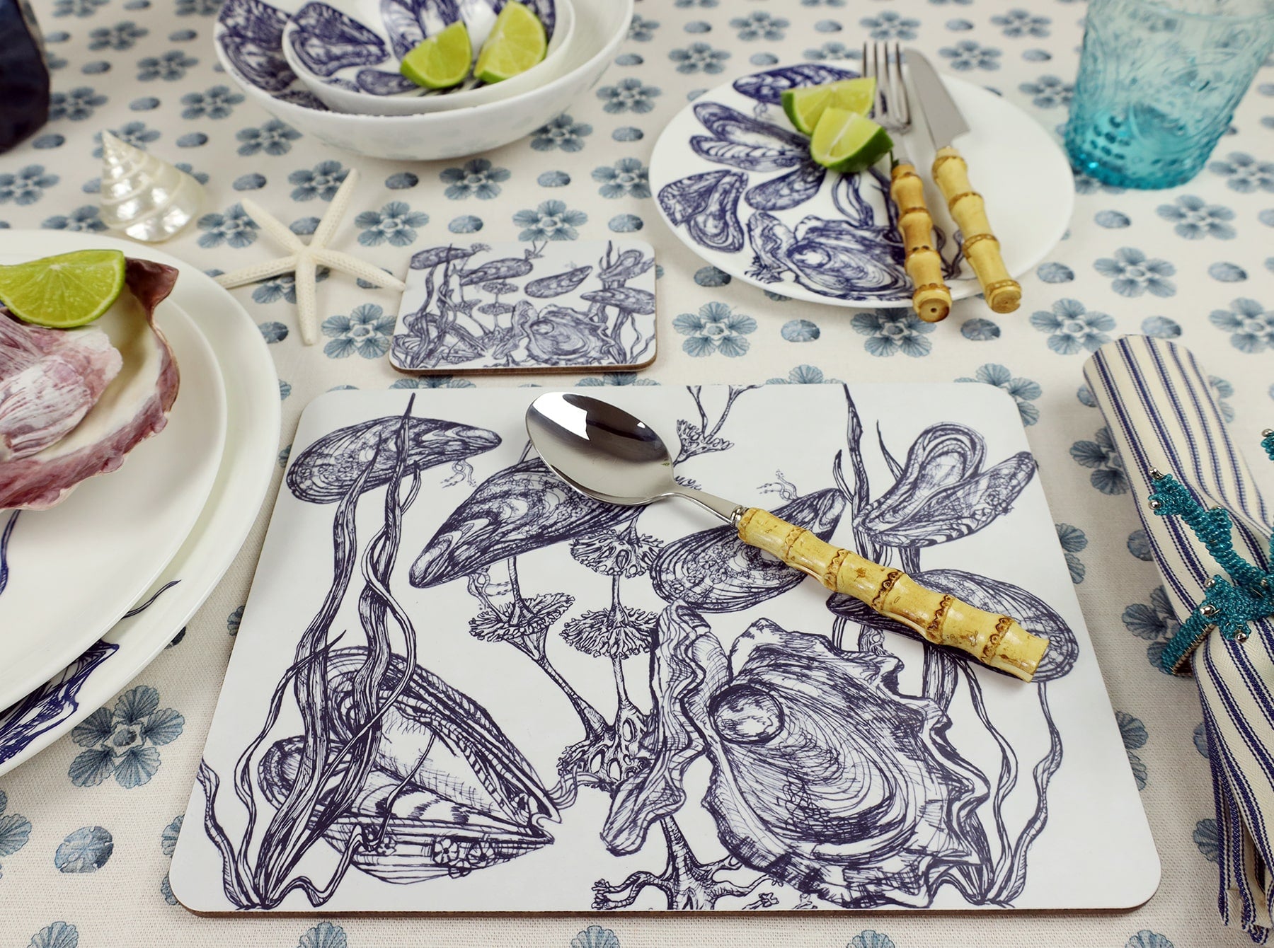 Mussel and Oyster Design in Navy on a white Coaster with a matching Placemat on a Seastar printed tablecloth,also on the table are other tableware and bamboo tableware.