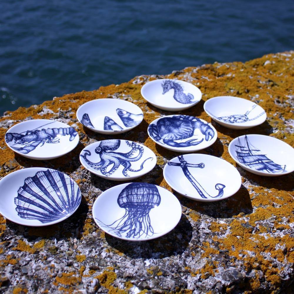 Nibbles bowl in Bone China in our Classic range in Navy and white in the Lobster design outside on a lichen covered wall.Surrounding the bowl are 9 other various nibbles bowls