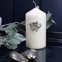 Pewter Octopus Candle Pin decoration placed onto a thick white candle placed on a table next to other Pewter items