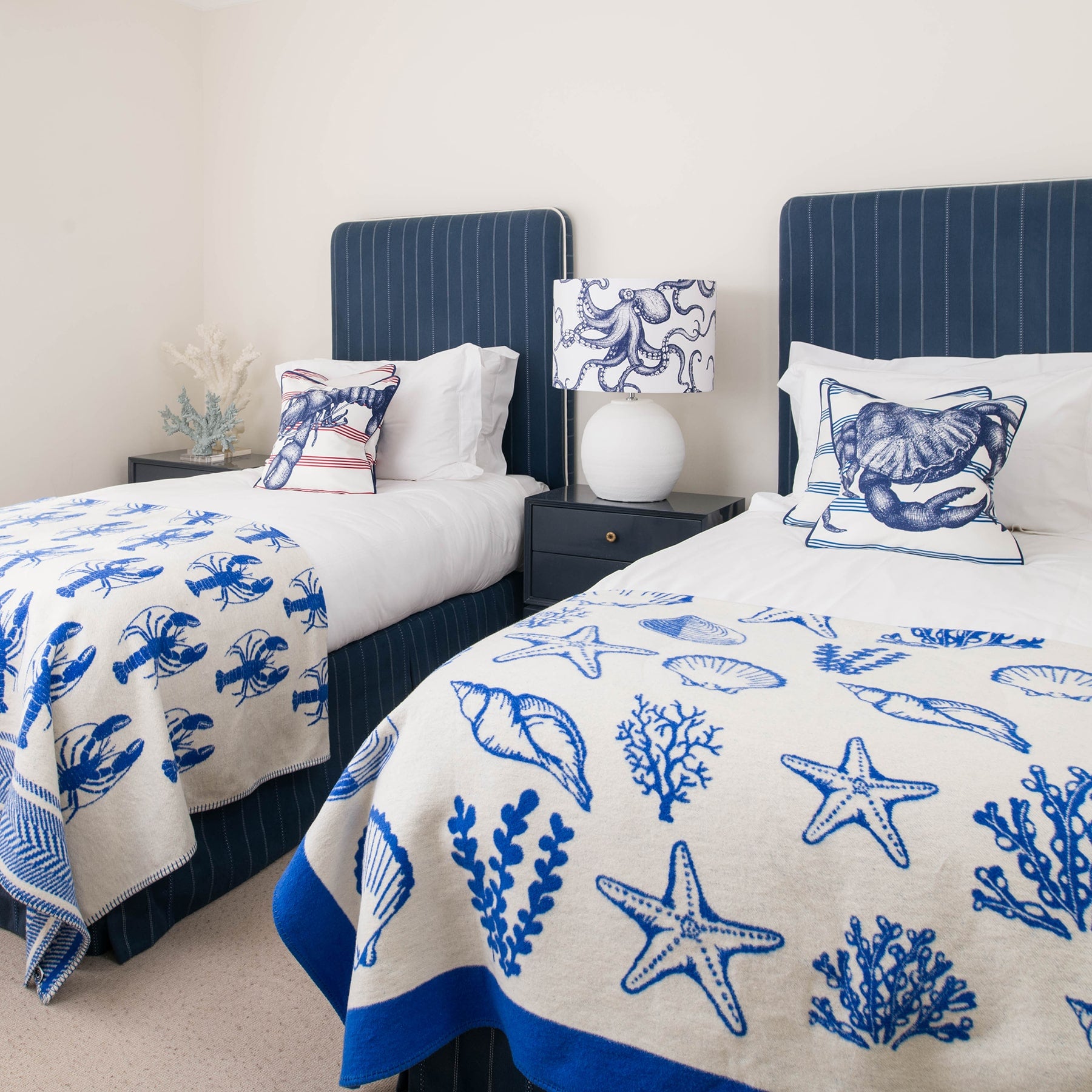 Our Classic Navy Octopus design on a white background on a white lampbase on a side table between two single beds.On the beds are classic Navy and White cushions and our reversible throws are draped over the ends of the beds.