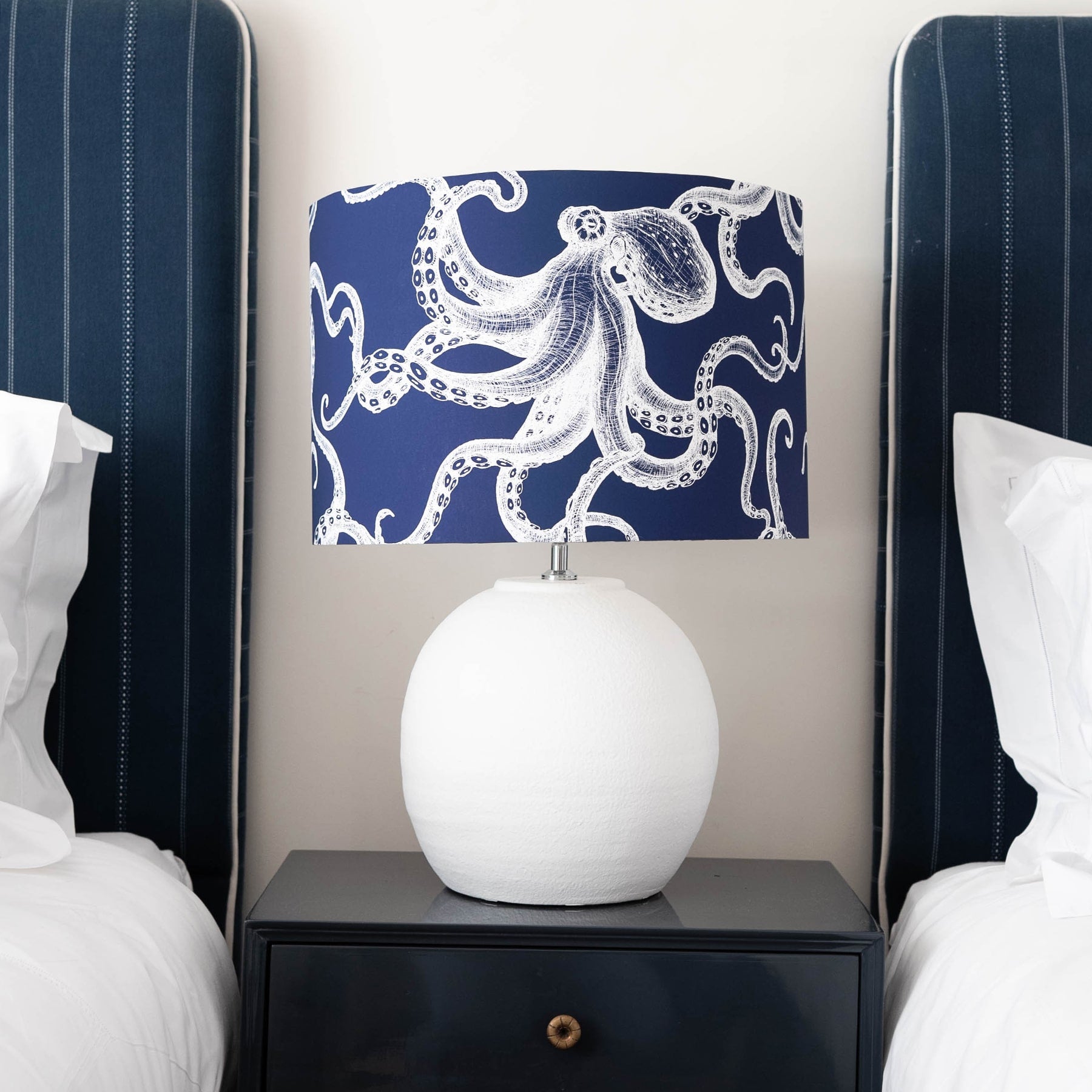 Our Classic Octopus White design on a Navy background on a White lampbase placed on a navy bedside table in between two single beds.