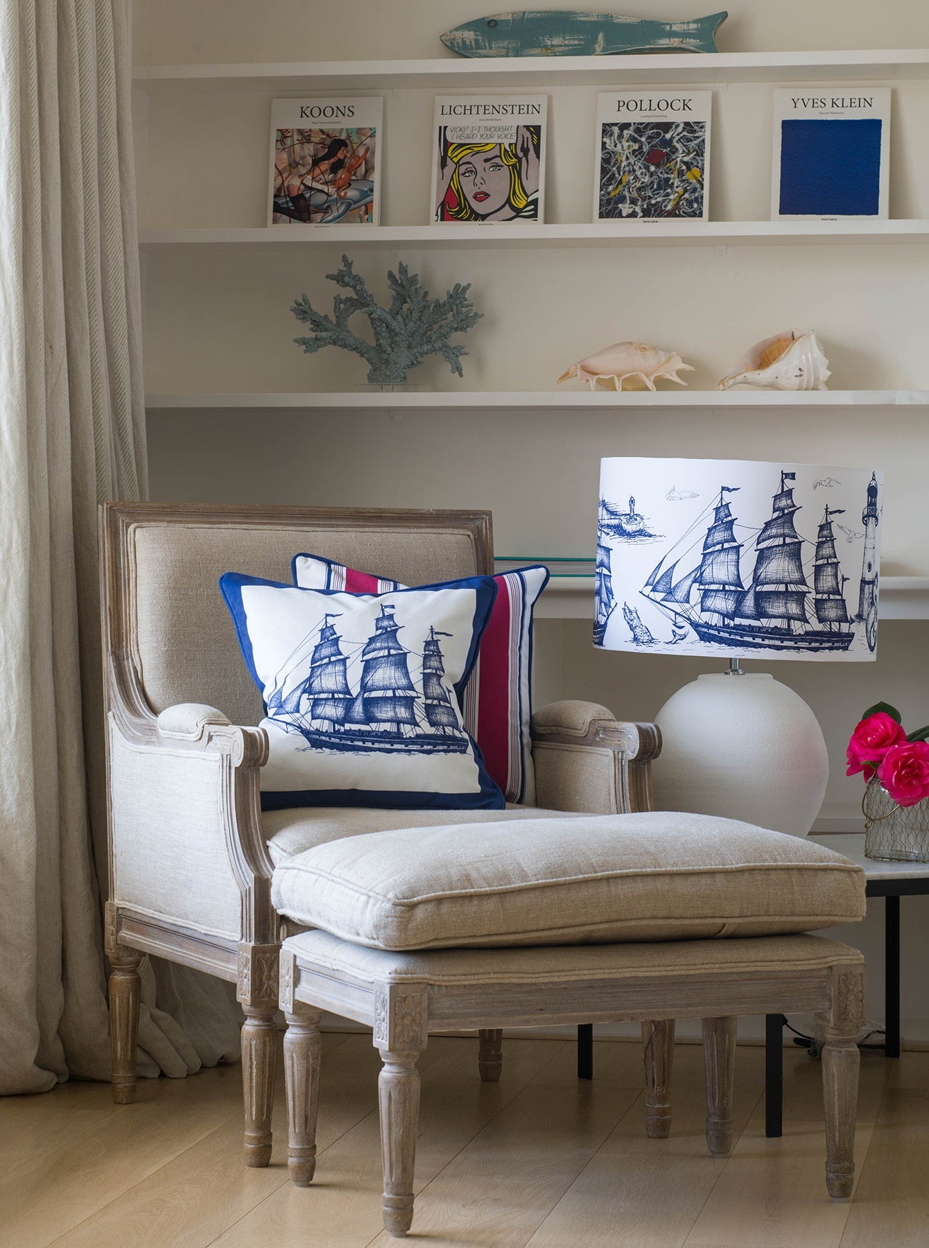 Our Classic Navy Maritime design on a white background on a lampbase on a side table next to a chair and matching footstool.Behind the chair is a bookcase with art books, coral and shells on the shelves