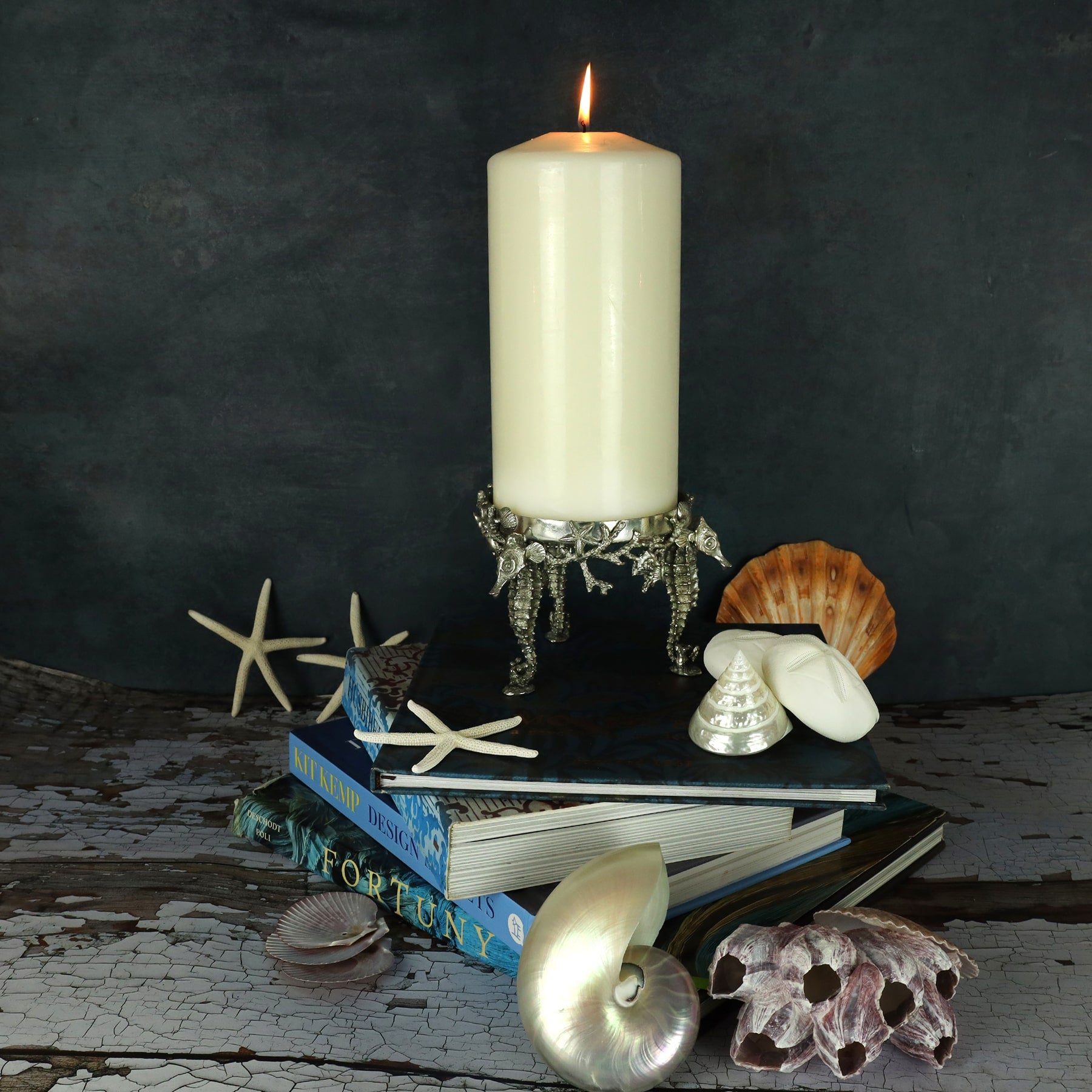 Front shot of large Pewter Candle Holder featuring intricate seahorses all placed on books with shells on the table