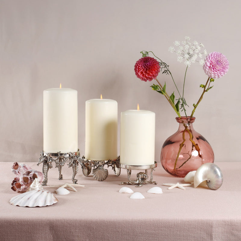 Shells & Coral  Candle Holder holding a large candle.Also next to this are 2 other candle holders with candles.Next to the items is a vase containing flowers