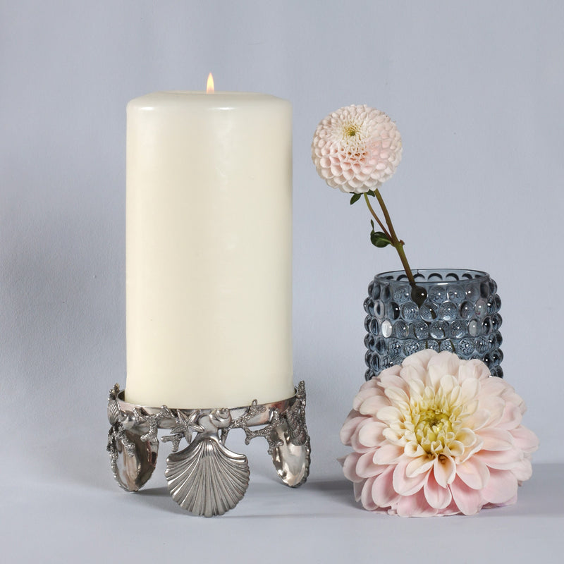 Shell & Coral  Candle Holder holding a large candle,the shells are holding up the candle.Next to the item is a glass containing flowers