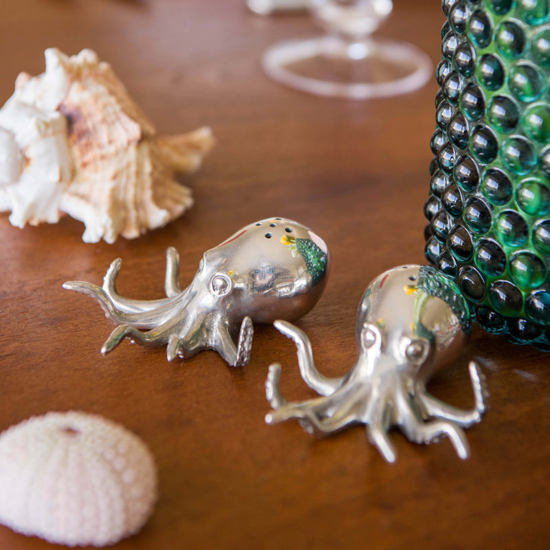 Pewter Octopus Salt and Pepper Shakers  placed on a table next to a glass vase and shells