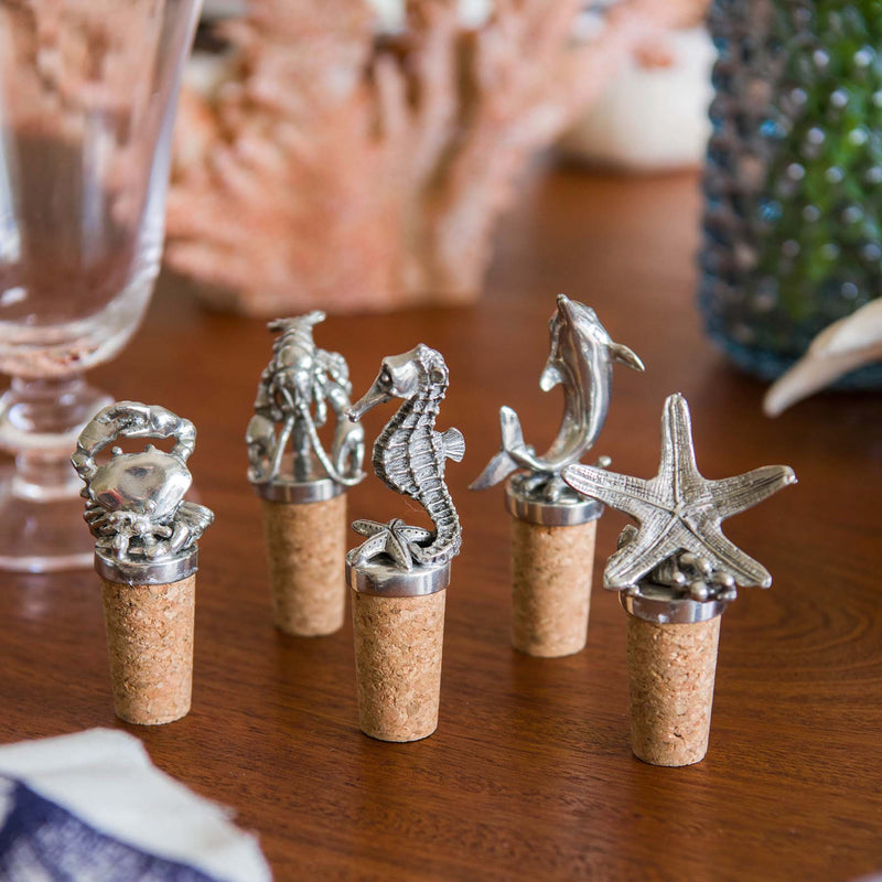 Seahorse,Starfish,Crab,Lobster and Dolphin Cork Stopper all lined up on a table with other items in the background