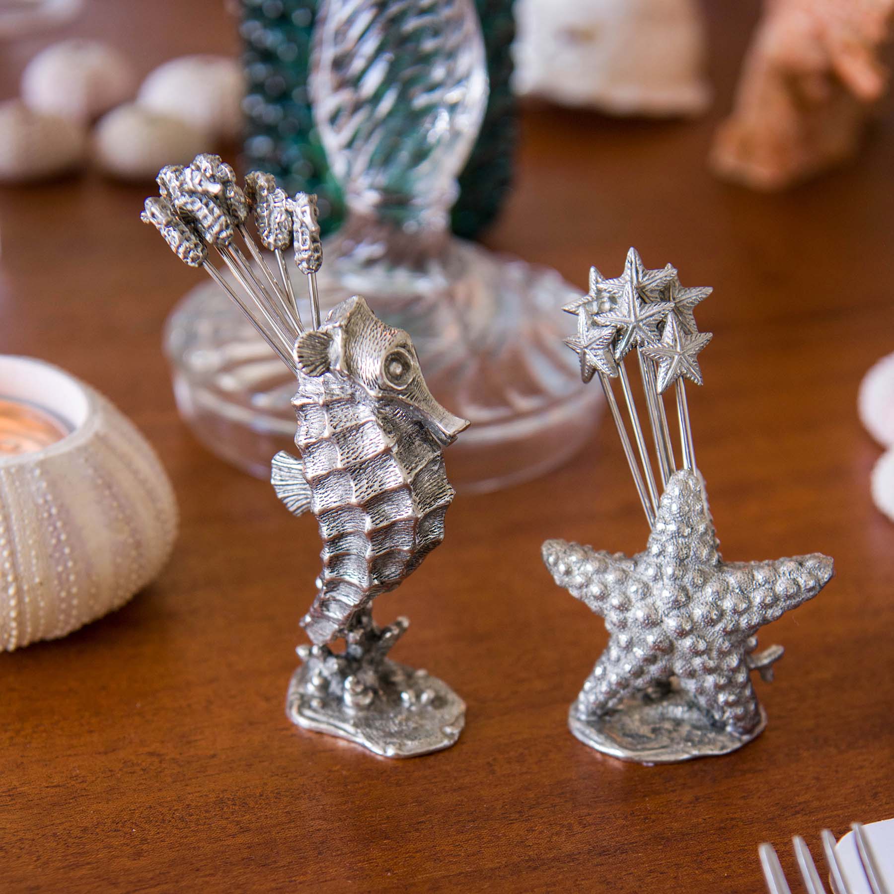 Pewter Seahorse shaped Pick Set with seahorses at one end of each of the picks placed on a table ,a glass and tableware can be seen surrounding it