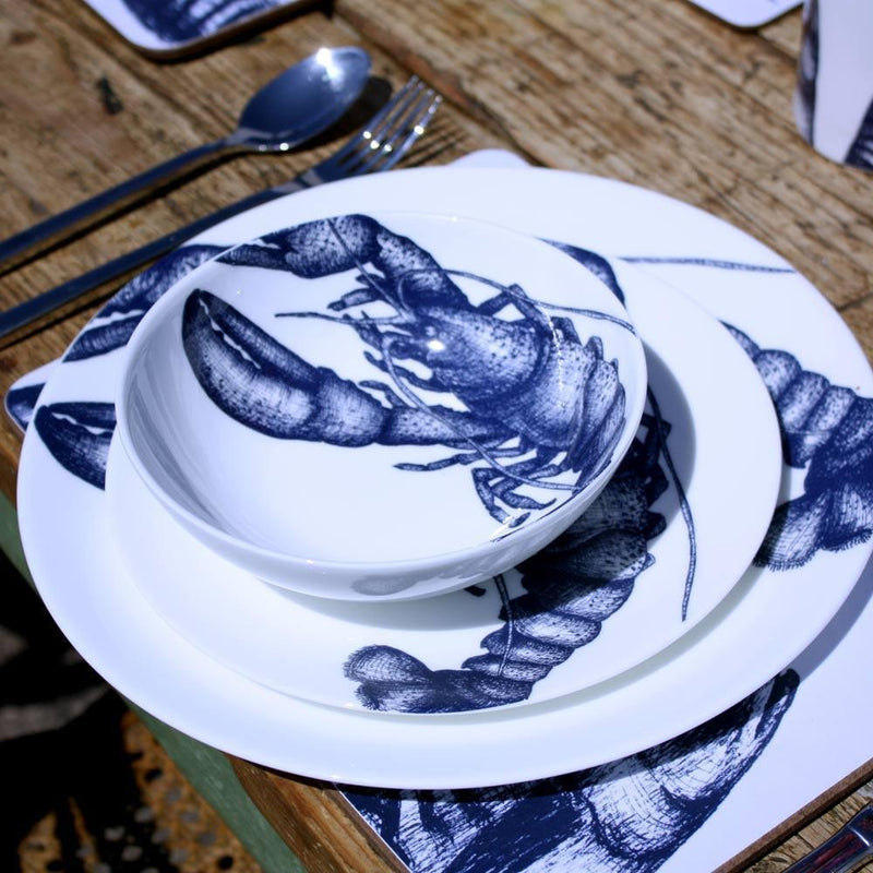 Outside Table setting with Large Lobster plates,stacked with the bowls on a placemat,next to a coaster with a blue glass.