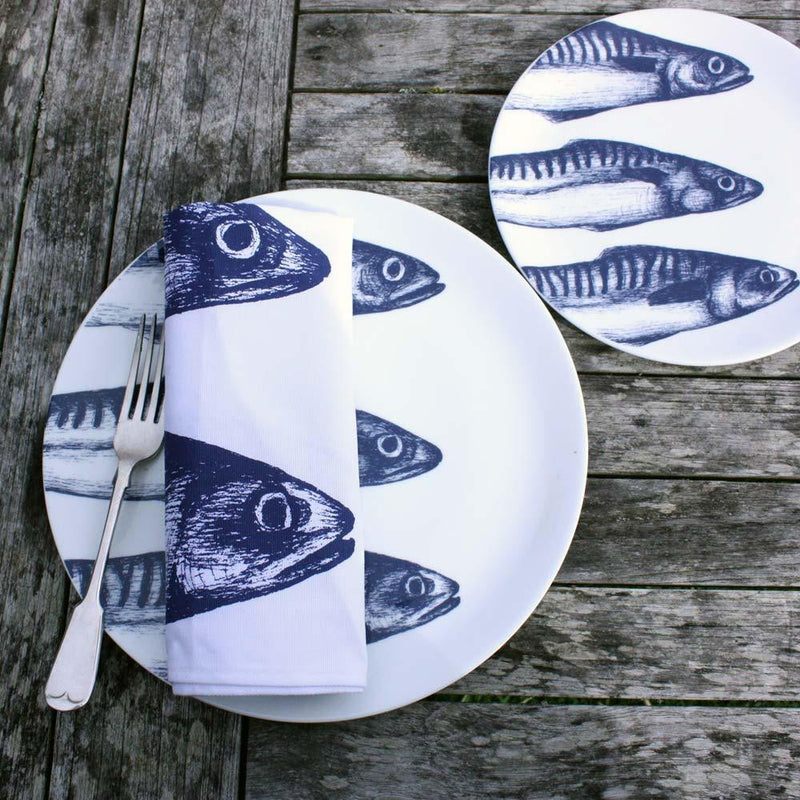 Aerial view of Bone China White plate with hand drawn illustration of our Mackerel heads in Navy with a fork and napkin.Next to the dinner plate is a side plate