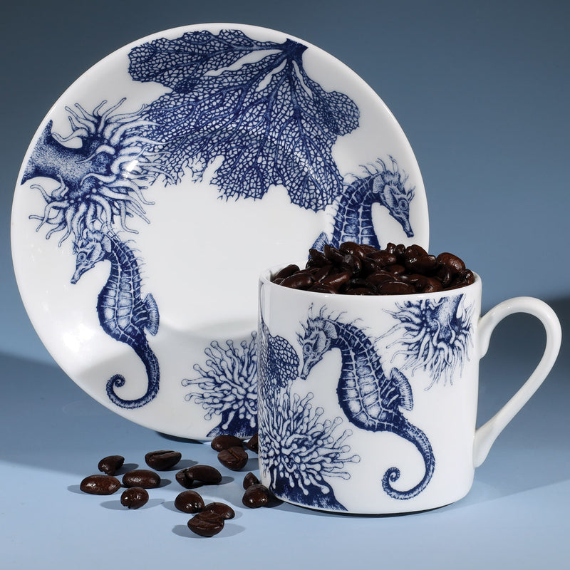 Bone China white espresso cup in hand drawn illustration in our Seahorse design in Navy with matching saucer.Saucer is standing on its side with the coffee cup in front filled with coffee beans
