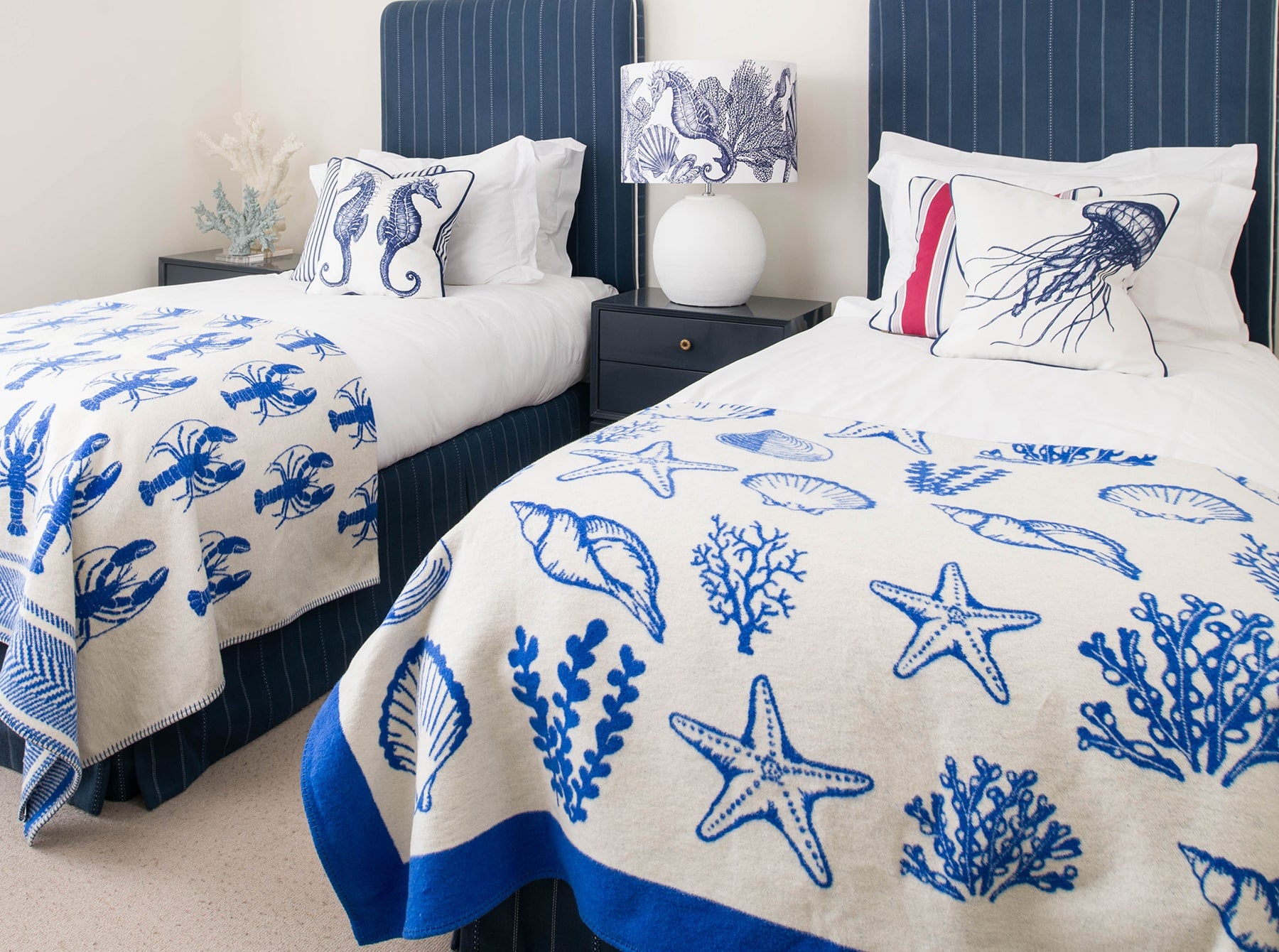 Our Classic Navy Seahorse design on a white background on a white lampbase on a side table between two single beds.On the beds are classic Navy and White cushions and our reversible throws are draped over the ends of the beds.