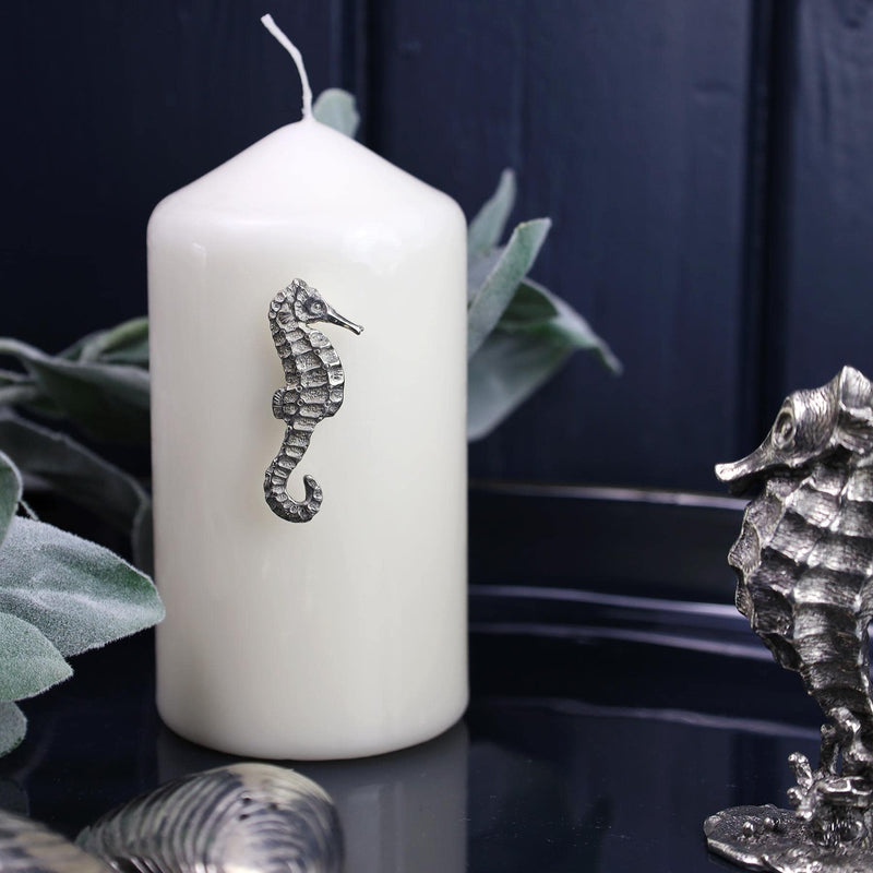 Pewter Seahorse Candle Pin decoration placed onto a thick white candle placed on a table next to other Pewter items