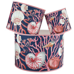 Shell Seeker Ink Blue Shade With Shells,Seaweed,Sea Urchin and Whelks Design in pinks/whites with a pink trim on the edge of the shade.The lampshades are shown in a stack of three showing all three sizes.