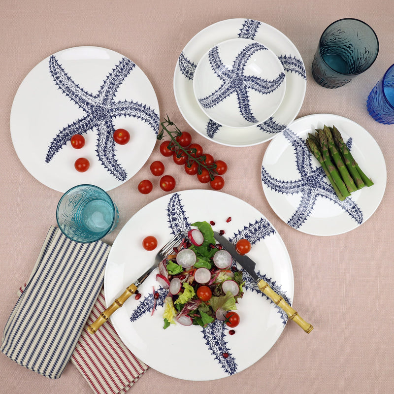 Pasta bowl in Bone China in our Classic range in Navy and white in the Starfish design next to a matching dinner plate and others decorated with brightly coloured food on a blush covered tablecloth