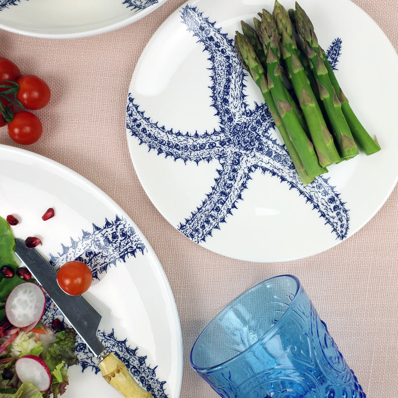 Aerial view of Starfish plate on a soft pink tablecloth.On the plate is a radish salad with Bamboo cutlery,to the side is another starfish plate with asparagus placed on it