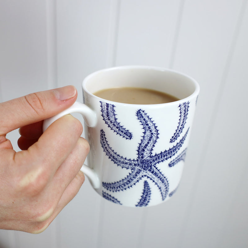 Bone china white mug featuring hand drawn Starfish design in classic Navy containing tea being held  