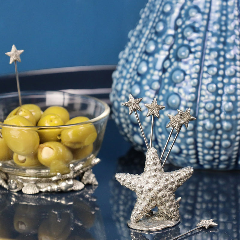 Pewter Starfish shaped Pick Set with starfish at one end of each of the picks placed on a table in front of an urchin Jug and a condiment glass bowl containing olives