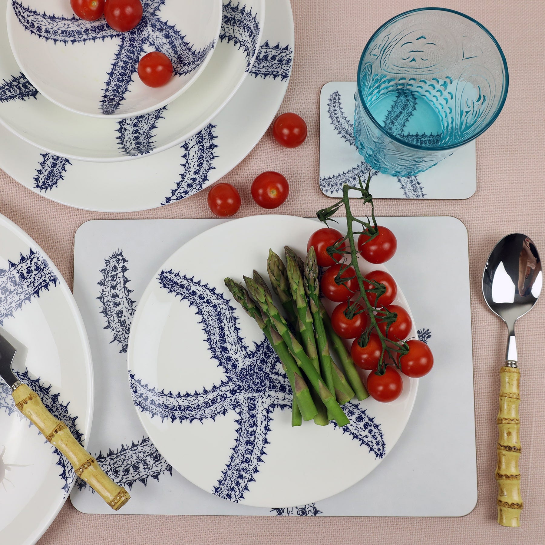 Starfish Placemat and matching Coaster placed on a table with bamboo cutlery.On the table is other tableware items,on the plates are tomatoes and some asparagus.