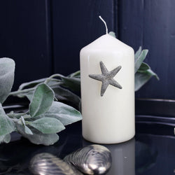 Pewter Starfish Candle Pin decoration placed onto a thick white candle placed on a table next to other Pewter items
