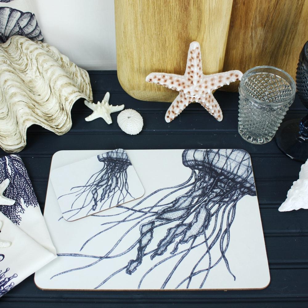 Jellyfish Design in Navy on a white Coaster with a matching Placemat.On the table are decorative shells and a matching napkin
