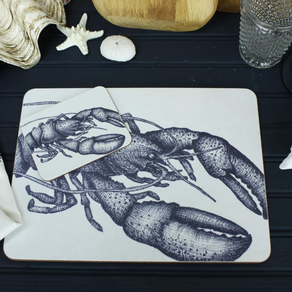 Lobster Design in Navy on a white Coaster with a matching Placemat.On the table are decorative shells and a matching napkin