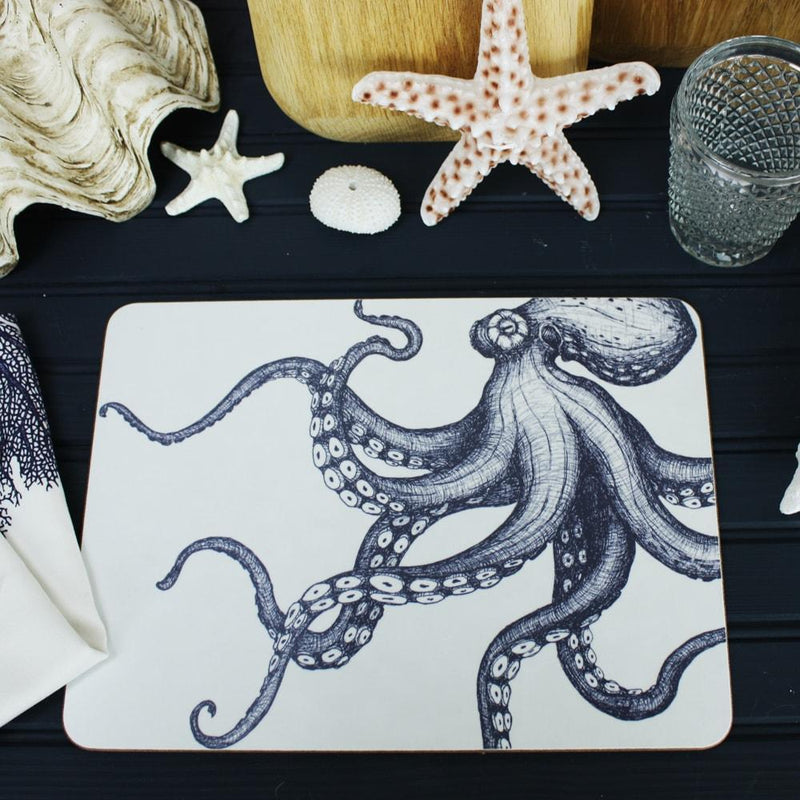 Octopus Design in Navy on a white Placemat .On the table are decorative shells,a clear glass and a matching napkin