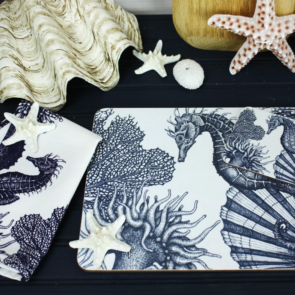 Seahorse Design in Navy on a white Coaster with a matching Placemat.On the table are decorative shells and a matching napkin