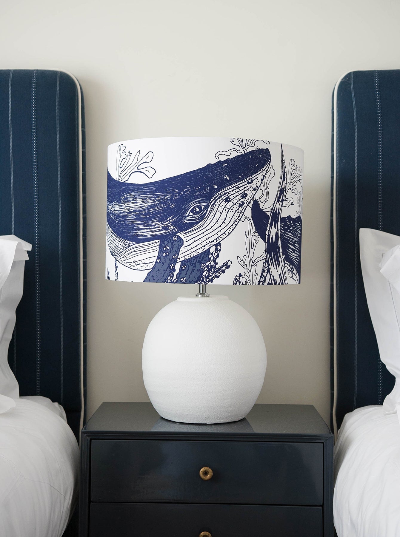 Our Classic Navy Whale design on a white background on a white lampbase on a side table in between two single beds