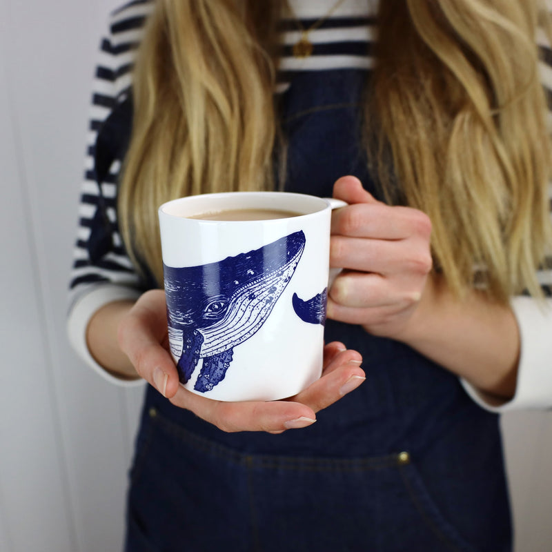 Bone china white mug featuring hand drawn Whale design in classic Navy held by a woman containing hot tea