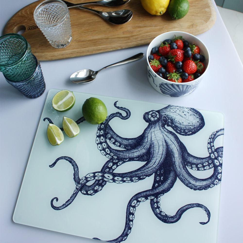 Worktop saver on toughened recycled glass with our Octopus design placed on a table with coloured glasses,a wooden board,fruits and a bowl on the table