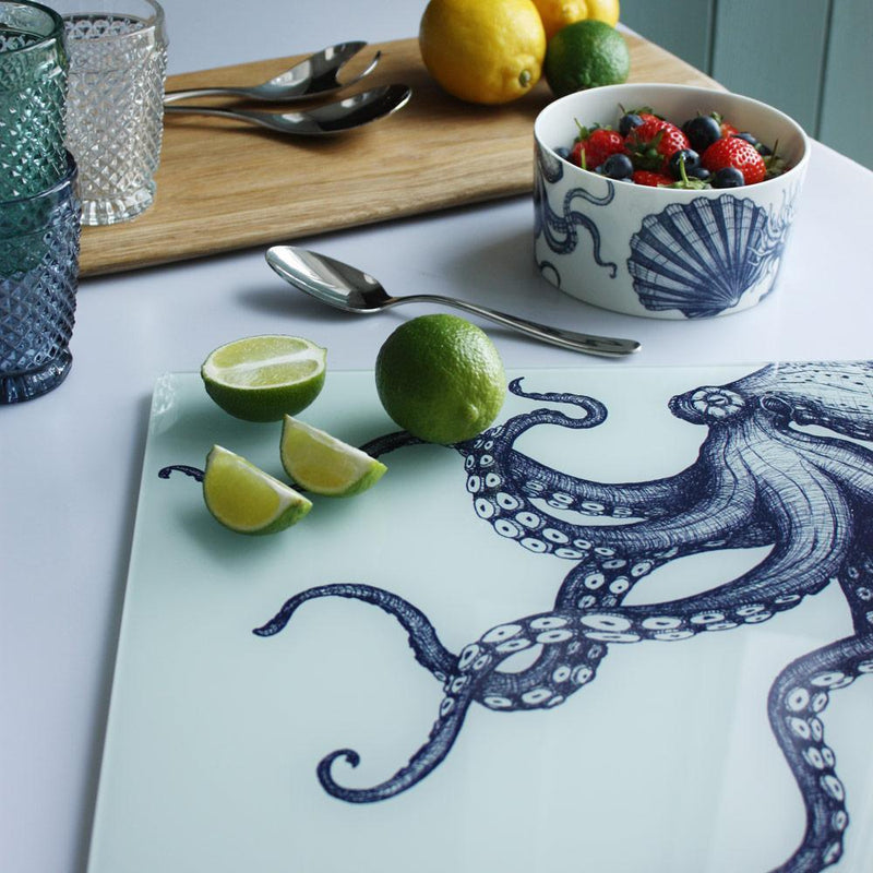 Close up of Worktop saver on toughened recycled glass with our Octopus design placed on a table with coloured glasses,a wooden board,fruits and a bowl on the table