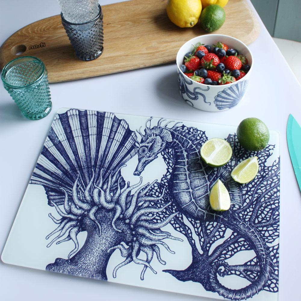 Worktop saver on toughened recycled glass with our Seahorse design placed on a table with coloured glasses,a wooden board,fruits and a bowl on the table