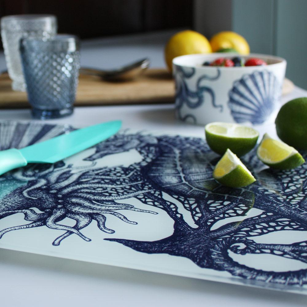 Close up of Worktop saver on toughened recycled glass with our Seahorse design placed on a table with coloured glasses,a wooden board,fruits and a bowl on the table